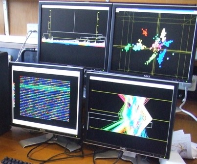 Four computer monitors displaying scientific data, including colourful cluster plots, graphs and a data matrix.